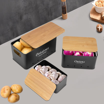 Schwarze Küchenaufbewahrungsboxen mit geöffneten Bambusdeckeln, befüllt mit Kartoffeln, Zwiebeln und Knoblauch.