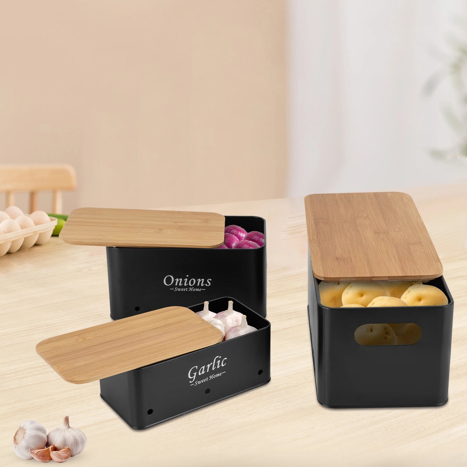 Schwarze Aufbewahrungsboxen für Zwiebeln, Knoblauch und Kartoffeln mit Bambusdeckeln auf Küchenarbeitsplatte.
