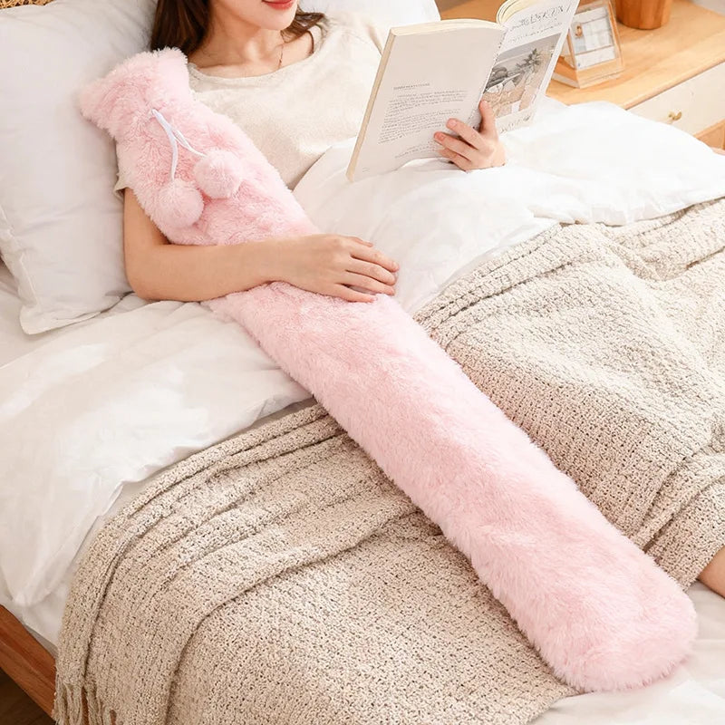 Extra lange Wärmflasche mit flauschigem Bezug in Pink liegt auf dem Bett – ideal zum Wärmen von Beinen und Bauch.