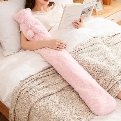 Extra lange Wärmflasche mit flauschigem Bezug in Pink liegt auf dem Bett – ideal zum Wärmen von Beinen und Bauch.