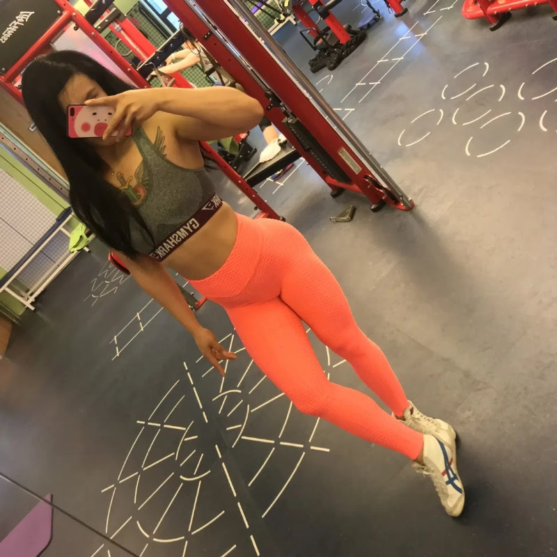 Neon-korallfarbene strukturierte Leggings bei einem Spiegelbild im Fitnessstudio.