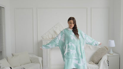 Video zeigt Frau in Oversize Hoodie Decke für Damen aus Fleece im Wohnzimmer – sie dreht sich, tanzt locker, hält einen Kaffeebecher und setzt sich gemütlich auf die Couch