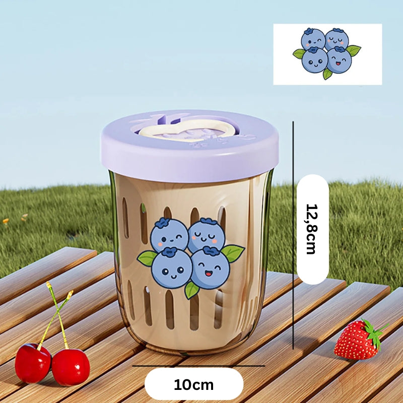 Sweet-Cherry-Fruchtbecher mit blauem Beerenmotiv und lila Deckel, auf Holztisch im Außenbereich mit Kirschen und Erdbeeren dekoriert.