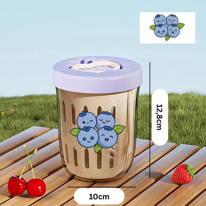 Sweet-Cherry-Fruchtbecher mit blauem Beerenmotiv und lila Deckel, auf Holztisch im Außenbereich mit Kirschen und Erdbeeren dekoriert.