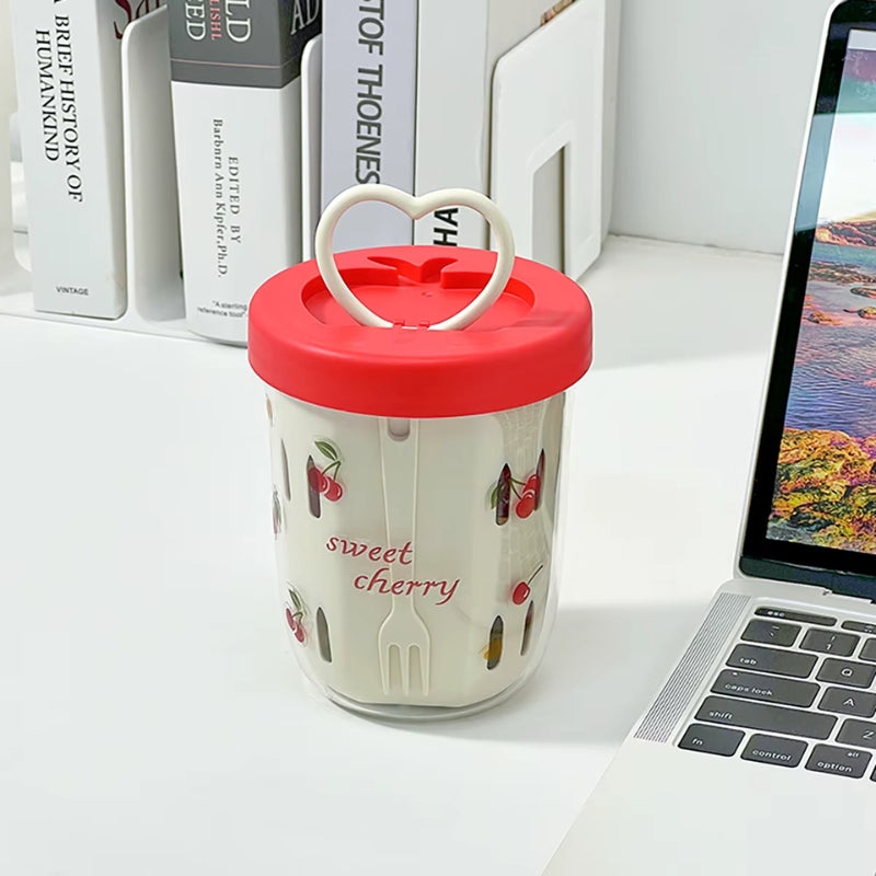 Sweet-Cherry-Salatbecher mit rotem Deckel und Herzgriff auf Schreibtisch neben Laptop und Büchern, modernes Alltagsdesign.