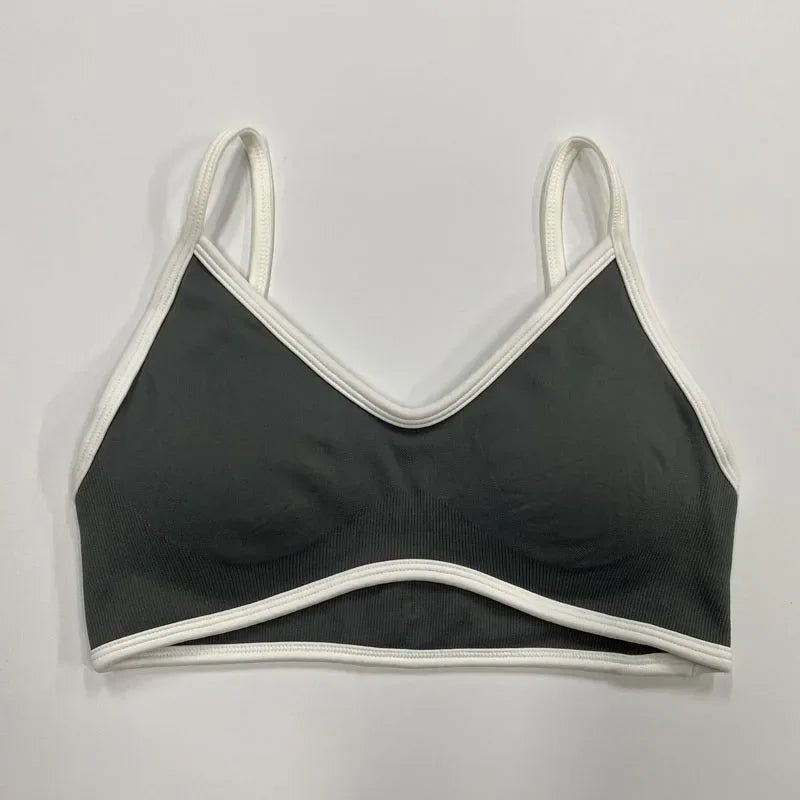 Dunkelgrauer nahtloser Damen Sport-BH mit weißen Abschlüssen und schmalen Trägern auf neutralem Hintergrund.