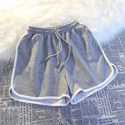 Graue Damen Sport Shorts mit elastischem Bund, weißer Paspelierung und Kordelzug auf Stoffuntergrund.