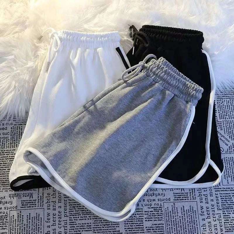 Übereinanderliegende Damen Sport Shorts in Grau, Weiß und Schwarz mit seitlicher Paspelierung.