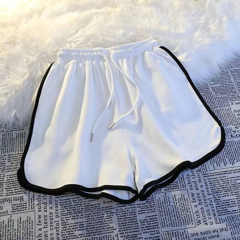 Weiße Damen Sport Shorts mit schwarzer Paspelierung und elastischem Bund auf Stoffuntergrund.